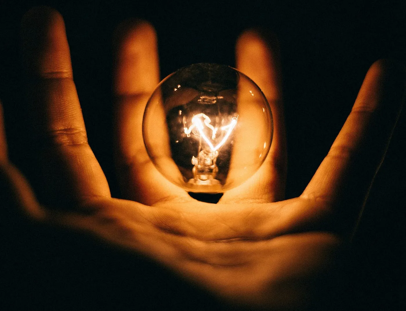 A glowing light bulb held against a dark background